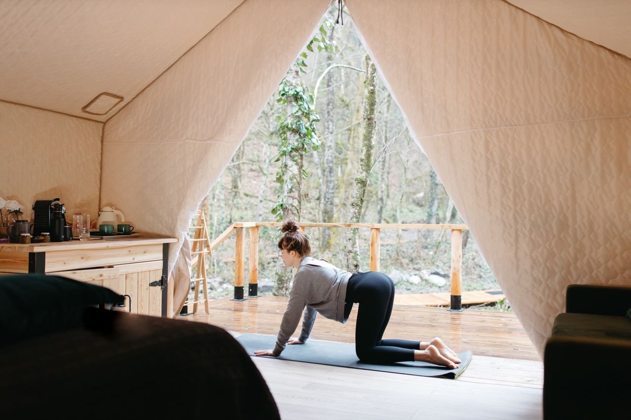 The Art of Drawing Readers In: Your attractive post title goes here A woman performs yoga inside a tent with a tranquil outdoor view, promoting wellness and relaxation.