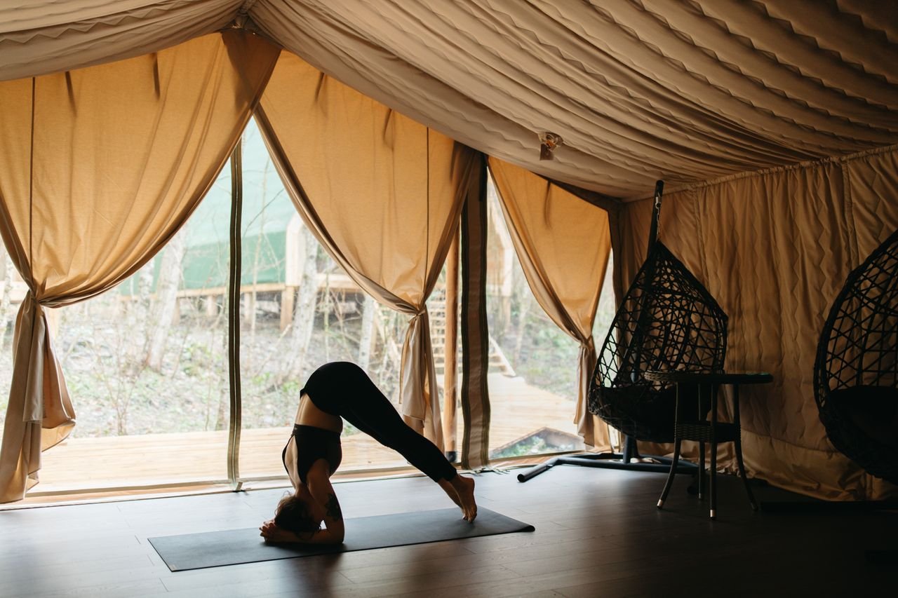 Adult woman performing yoga pose inside a tent with nature view, promoting serenity and wellness.